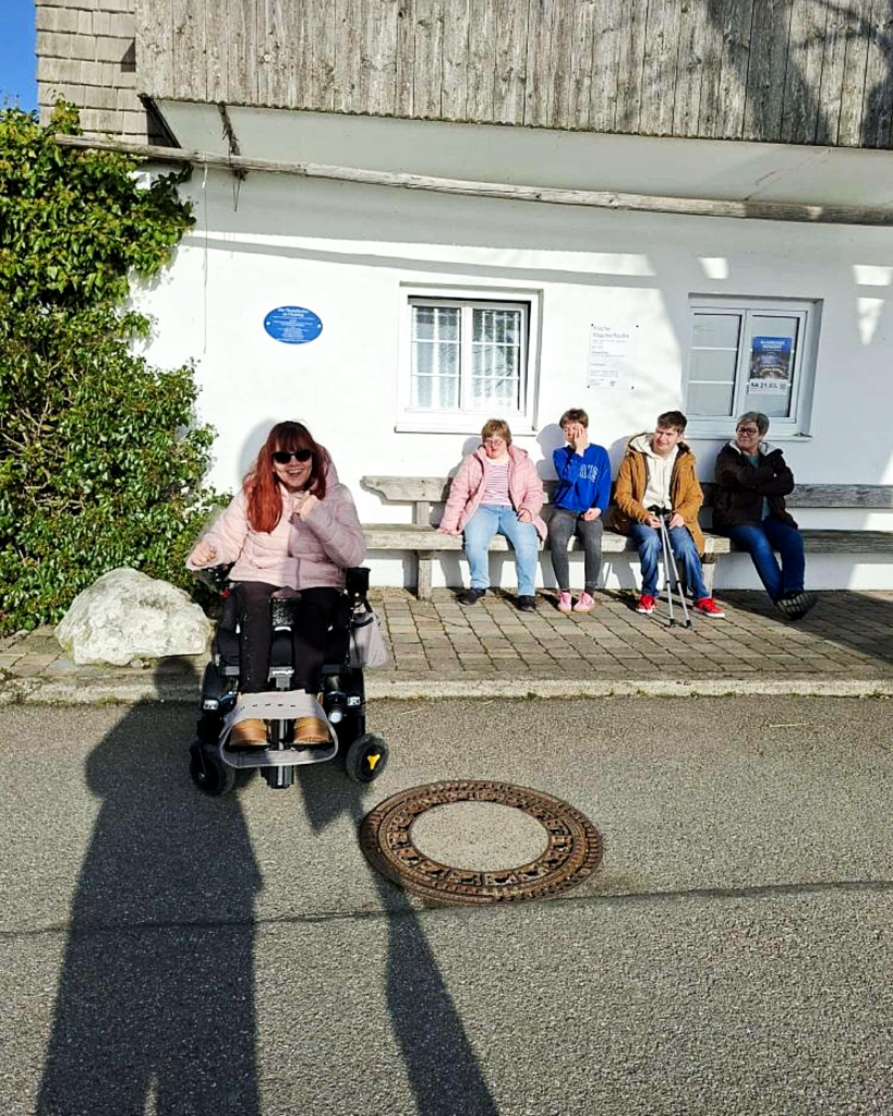 Vier Mitglieder der WG mit Herz und einer Betreuungsperson vor einem Haus